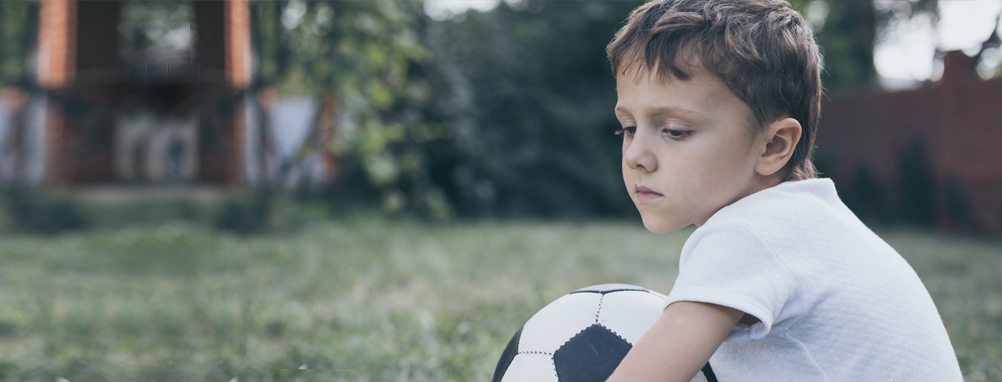 sad boy holding a soccer ball all alone.