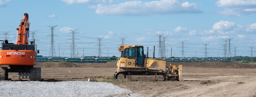 construction vehicles breaking ground on land with a go train passing in the distance.