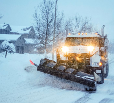 A snow plow driving down and plowing the road