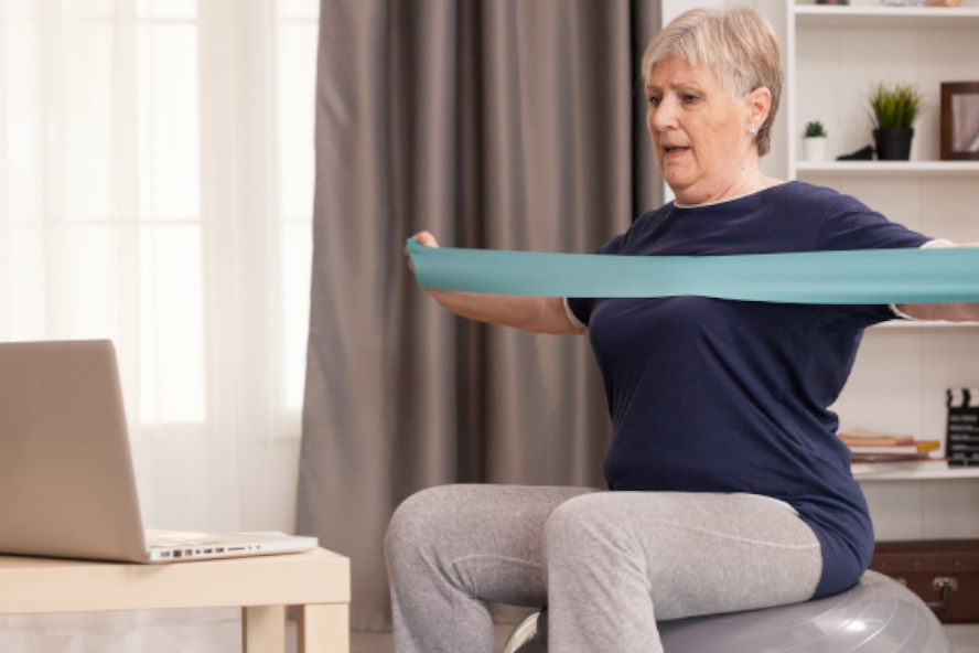 Older adult using tension band while seated on an exercise ball