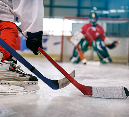 Hockey sticks and skates on the ice with a goalie net in the background