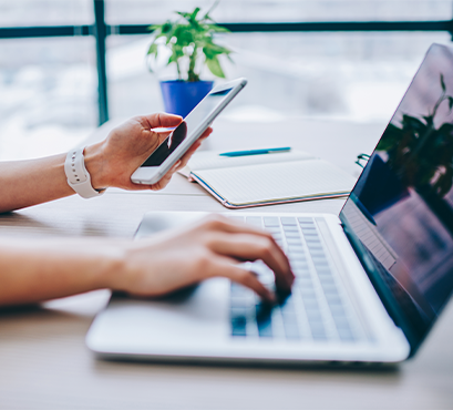 Hands holding a phone and typing on a laptop