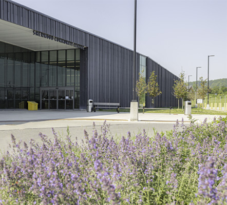 A building with the words Sherwood Community Centre on it with blue sky behind and purple flowers in the foreground