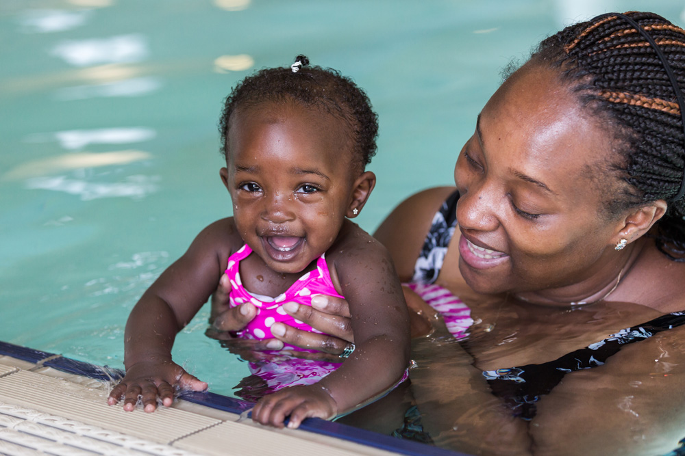 A woman holding a smiling baby in a pool