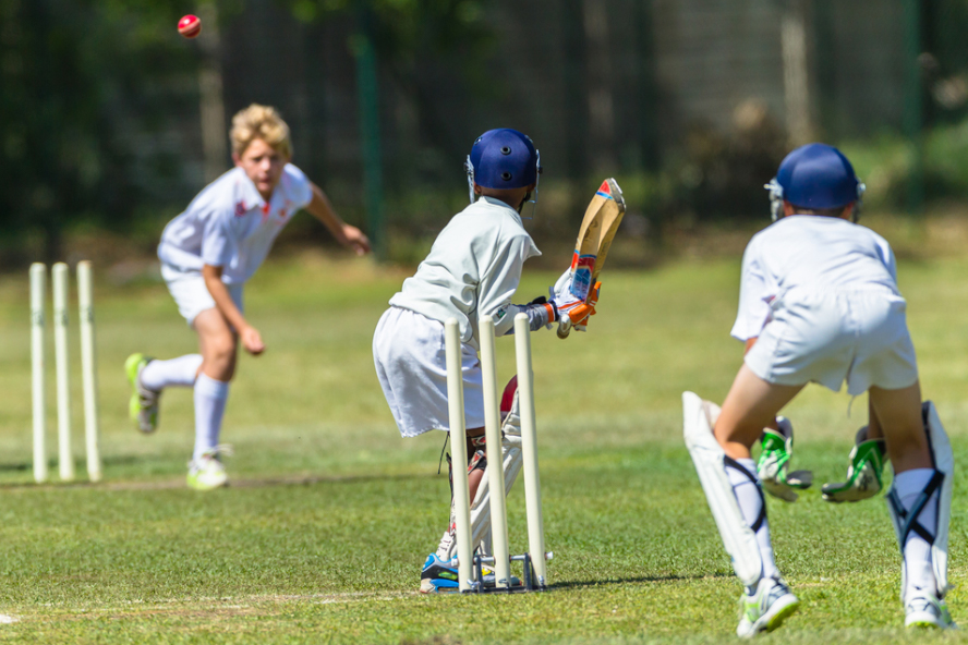 Three young people playing cricket