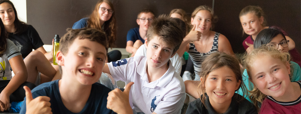 group of kids sitting, smiling with thumbs up