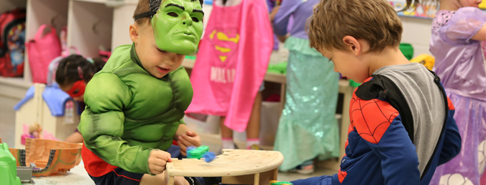 2 toddlers playing in super hero costumes on the mat in a pre-school class