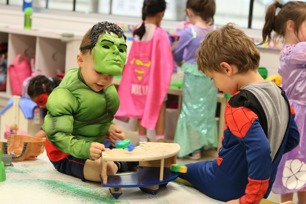 2 toddlers playing in super hero costumes on the mat in a pre-school class