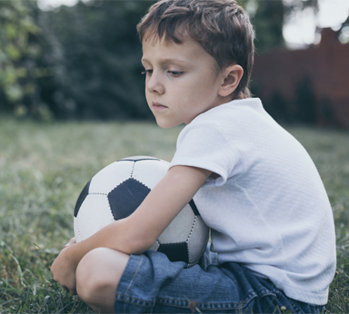 image of a boy sitting in the grass holding a soccer ball