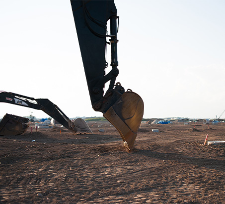 A backhoe digging into dirt with a blue sky behind