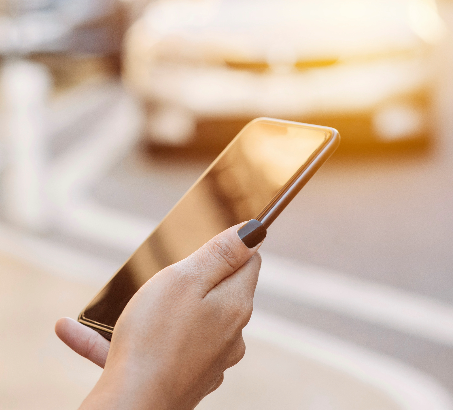 A person holding a cell phone with a car in the background