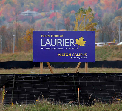 A purple Laurier sign with trees and cars in the background