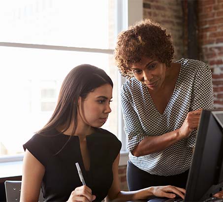 A mature woman mentoring a young woman at a computer 