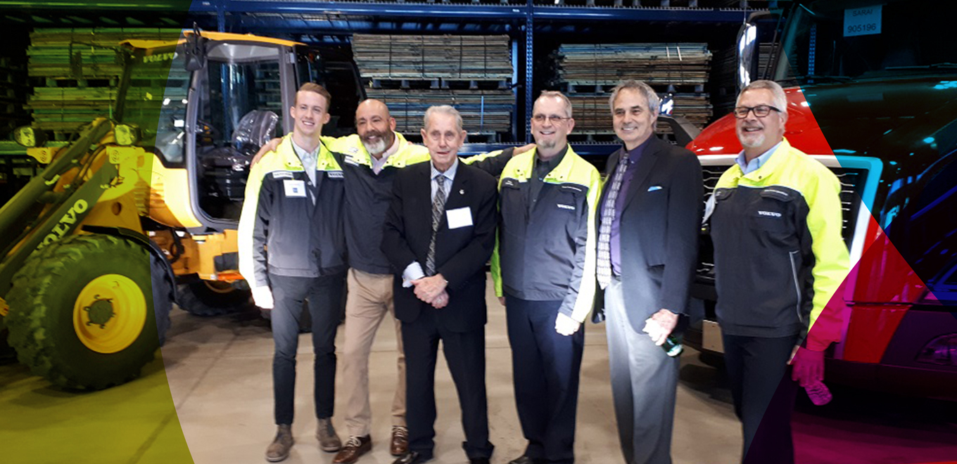 row of men in matching work coats posing in front of tractors