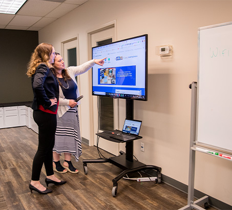 Two women standing at a large tv pointing at content on screen