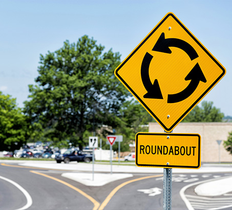 A yellow roundabout sign in front of a roundabout
