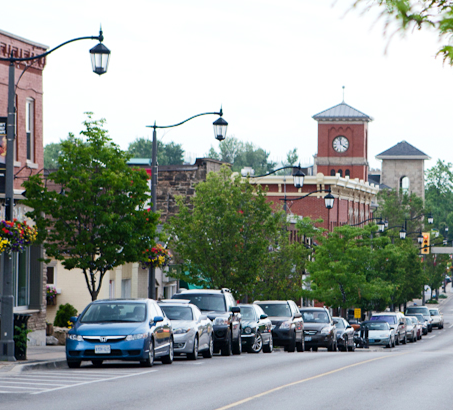 A row of cars parked on the street with trees and buildings behind