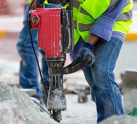 A road construction worker using a power tool for road work