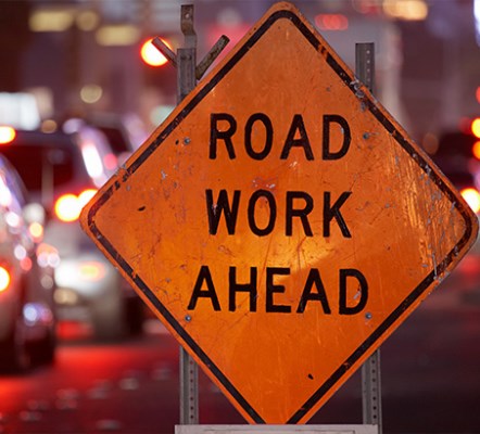 A road work ahead sign with tail lights in the background