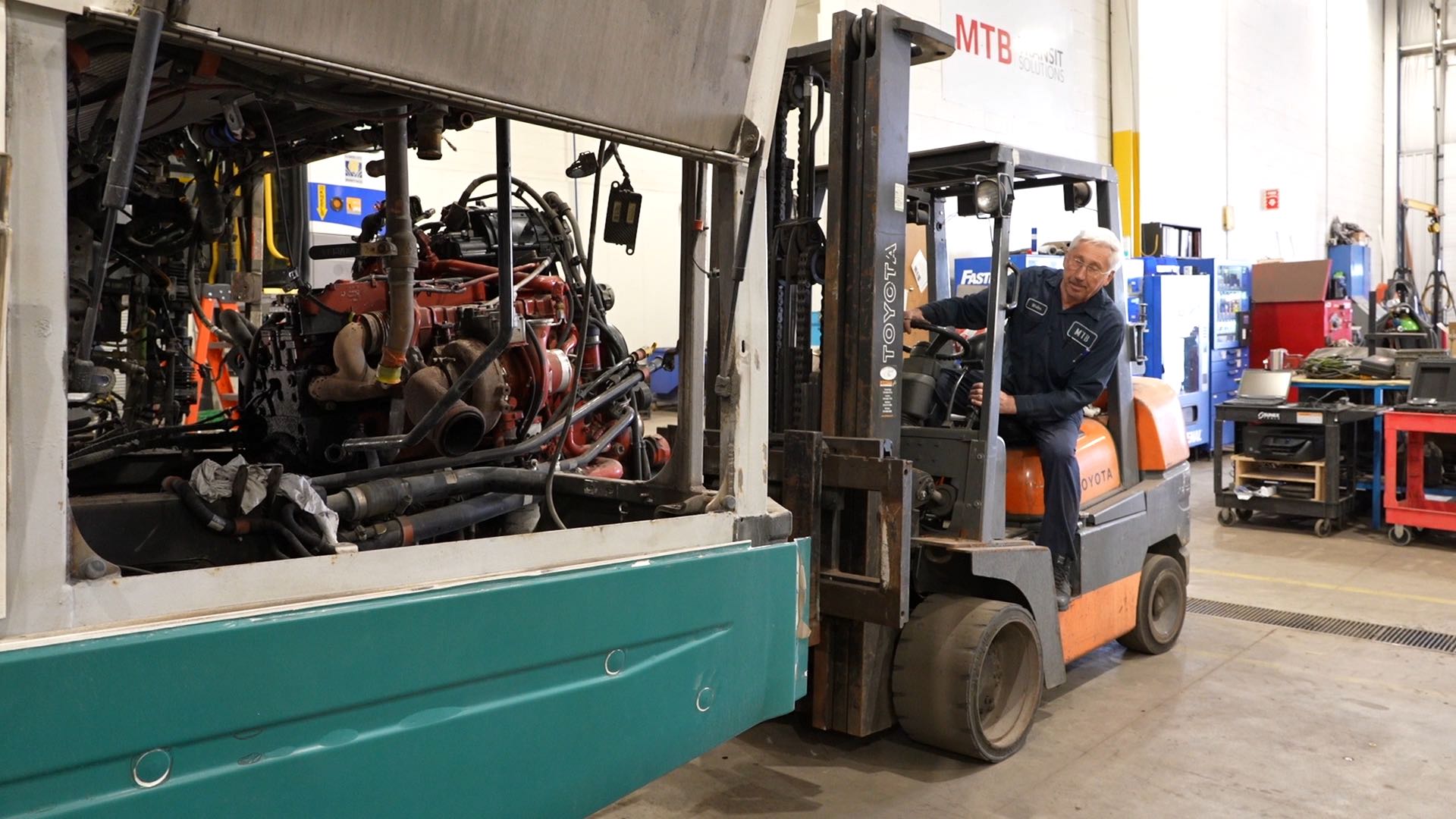 A man on a forklift removing the engine from a transit bus