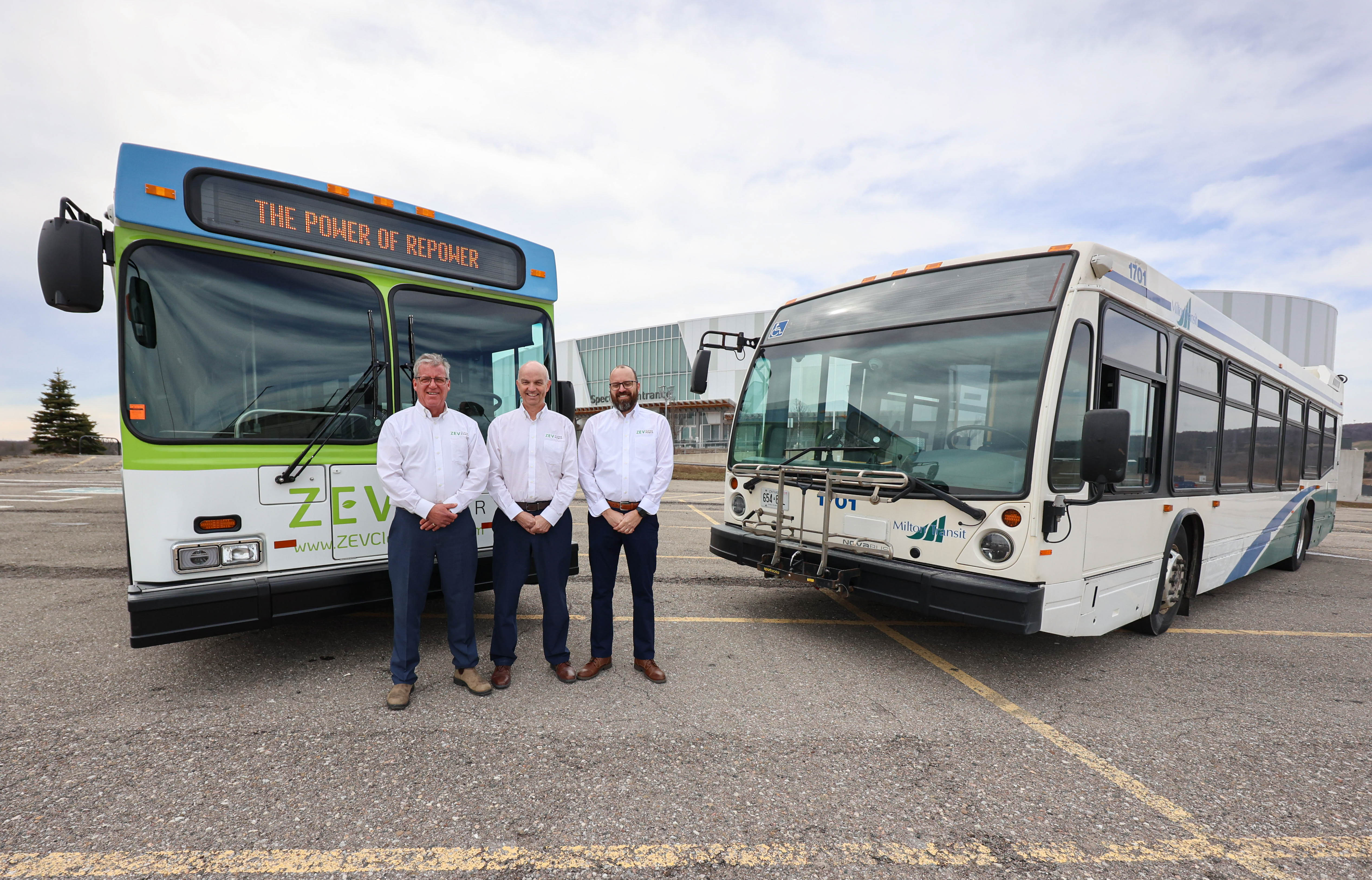 Three men standing in front of two parked buses