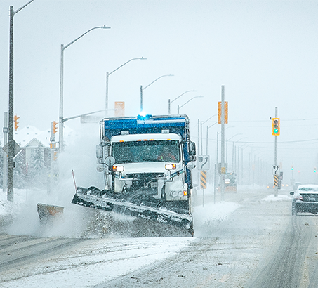 A snow plow driving down the road removing snow and ice from its path