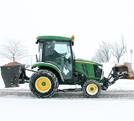 Small tractor salting an icy sidewalk