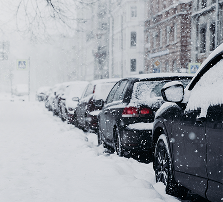 A line of cars parked on the street while it is snowing