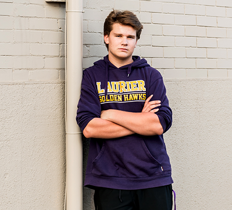 Male youth leaning against a brick wall wearing a sweatshirt