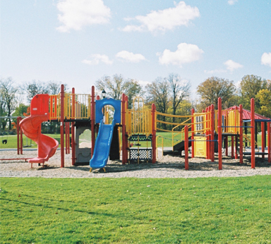 A playground at a park on a sunny day with clouds in the sky