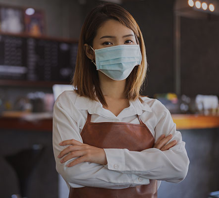 Professional woman in an apron wearing a face mask within a cafe