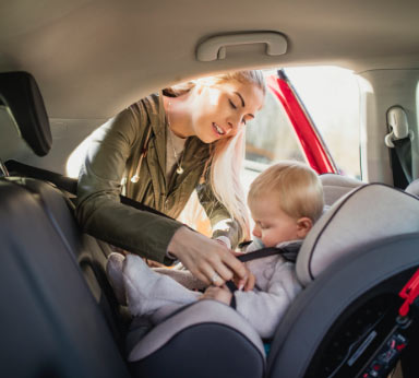 A woman putting a child into a car seat