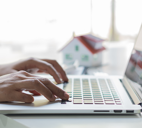 Hands typing on a laptop with a small house figure in the background