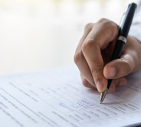 A hand holding a pen filling out a financial report