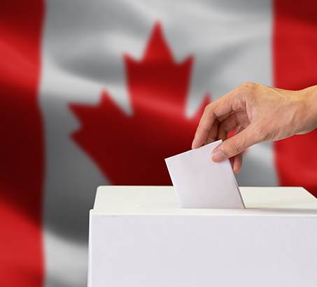 A hand dropping a ballot into a box with the Canada flag in the background