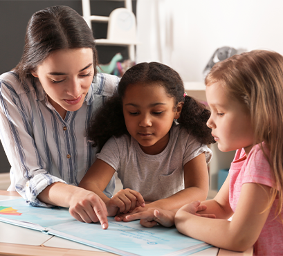 A woman helping two small girls at a table with papers